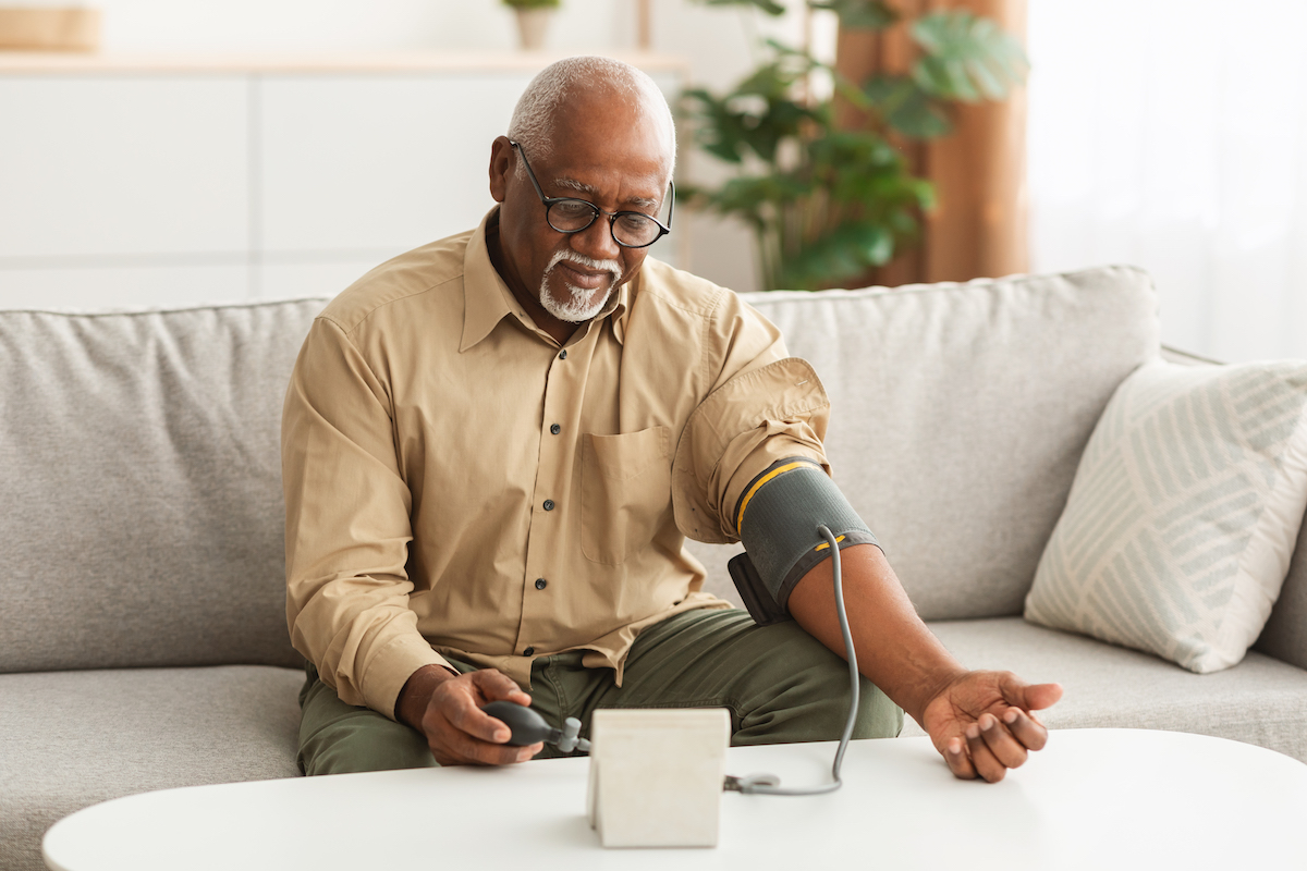Hypertension Problem In Senior Age. African American Man Measuring Arterial Blood Pressure Using Sphygmomanometer Cuff Sitting On Couch At Home.