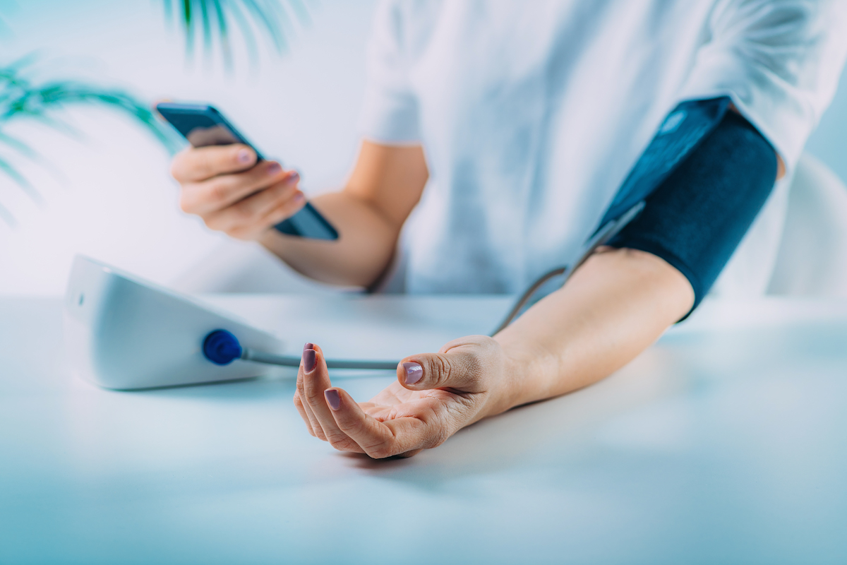 Foto på en person som mäter blodtrycket och håller sin mobiltelefon i andra handen.