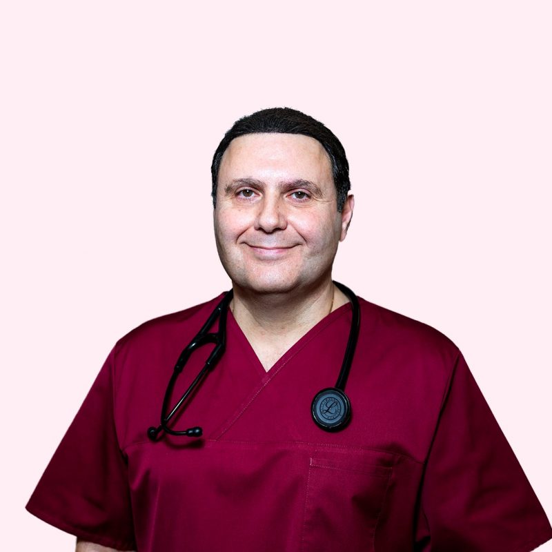 Bild på en läkare i vinröd uniform med ett stetoskop runt halsen mot en ljusrosa bakgrund.