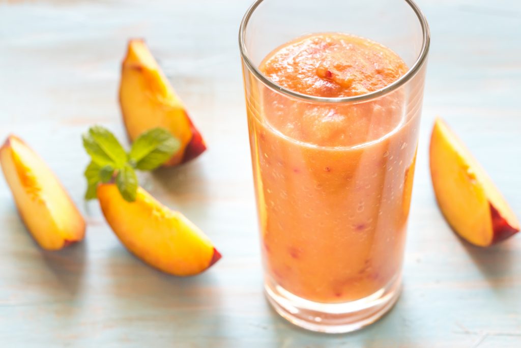 Ett glas smoothie med persika och några persikoklyftor intill glaset. 