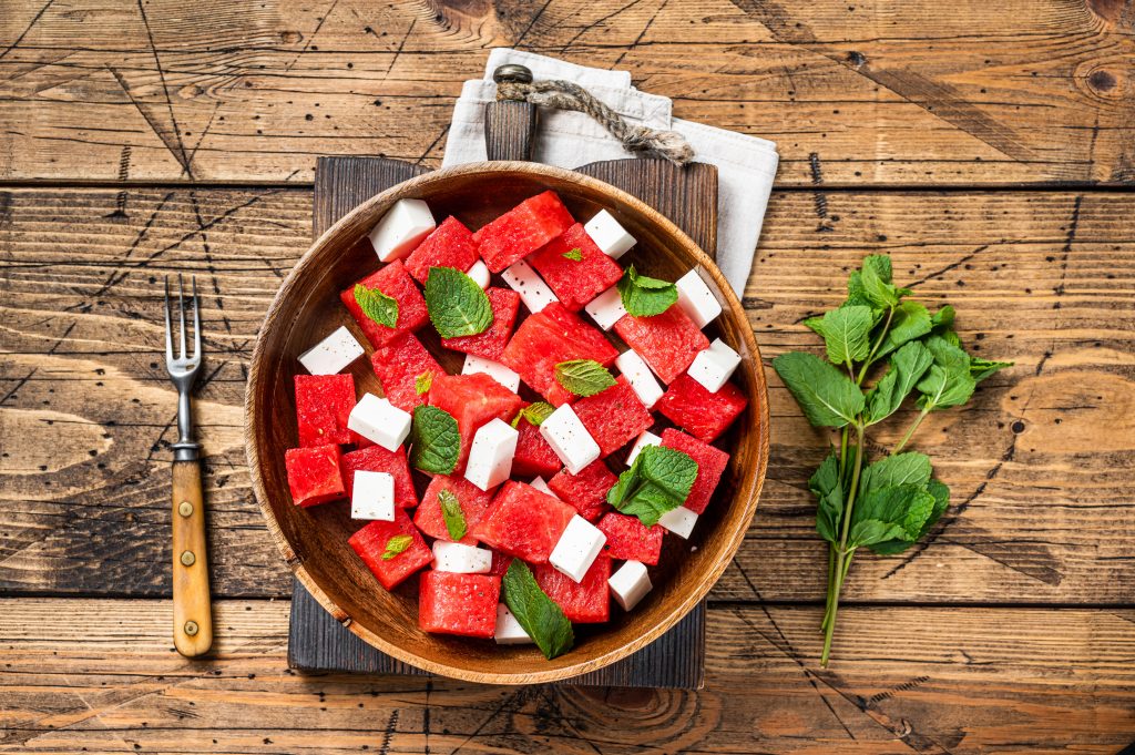 En skål med en sallad bestående av vattenmelon, mynta och fetaost, ståendes på ett trädbord. 