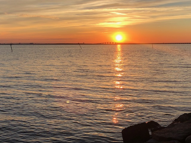 En solnedgång vid havet, himlen är orange och solen speglas i vattenytan.