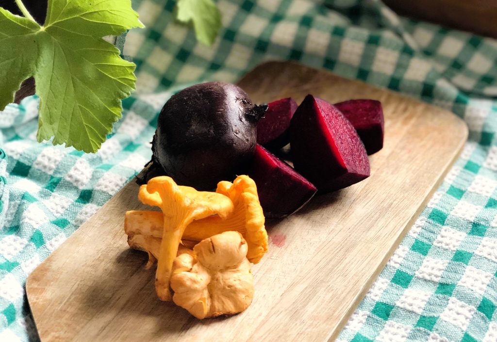 A boiled beetroot and chanterelle mushrooms on a wooden chopping board against a green and white checkered tea towel.