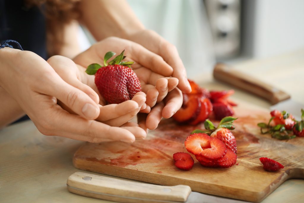 Bild på två barnhänder som håller en jordgubbe och som är omfamnade av två vuxenhänder.