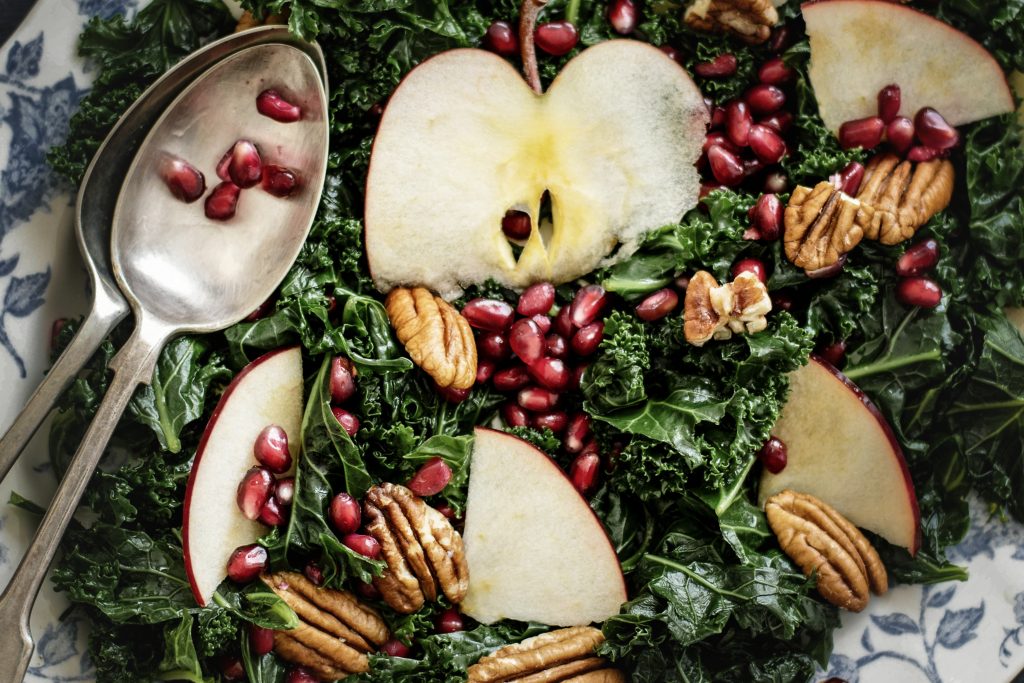 Bild på grönkålssallad toppad med äpplen, valnötter och granatäpplekärnor.