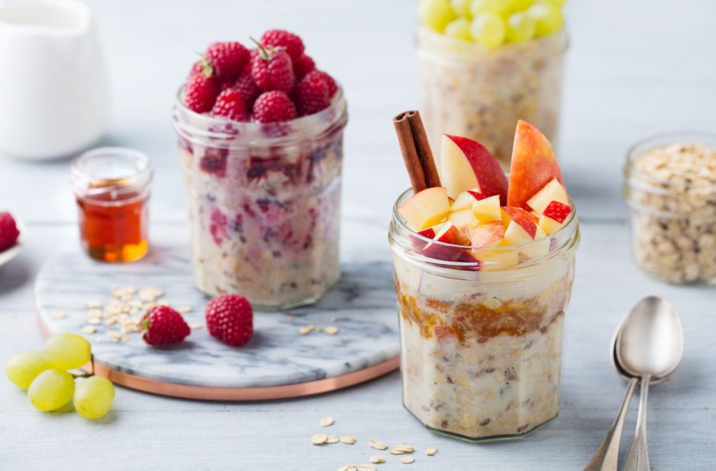 Tre burkar med overnight oats, toppade med frukter och bär, ståendes på ett bord. 