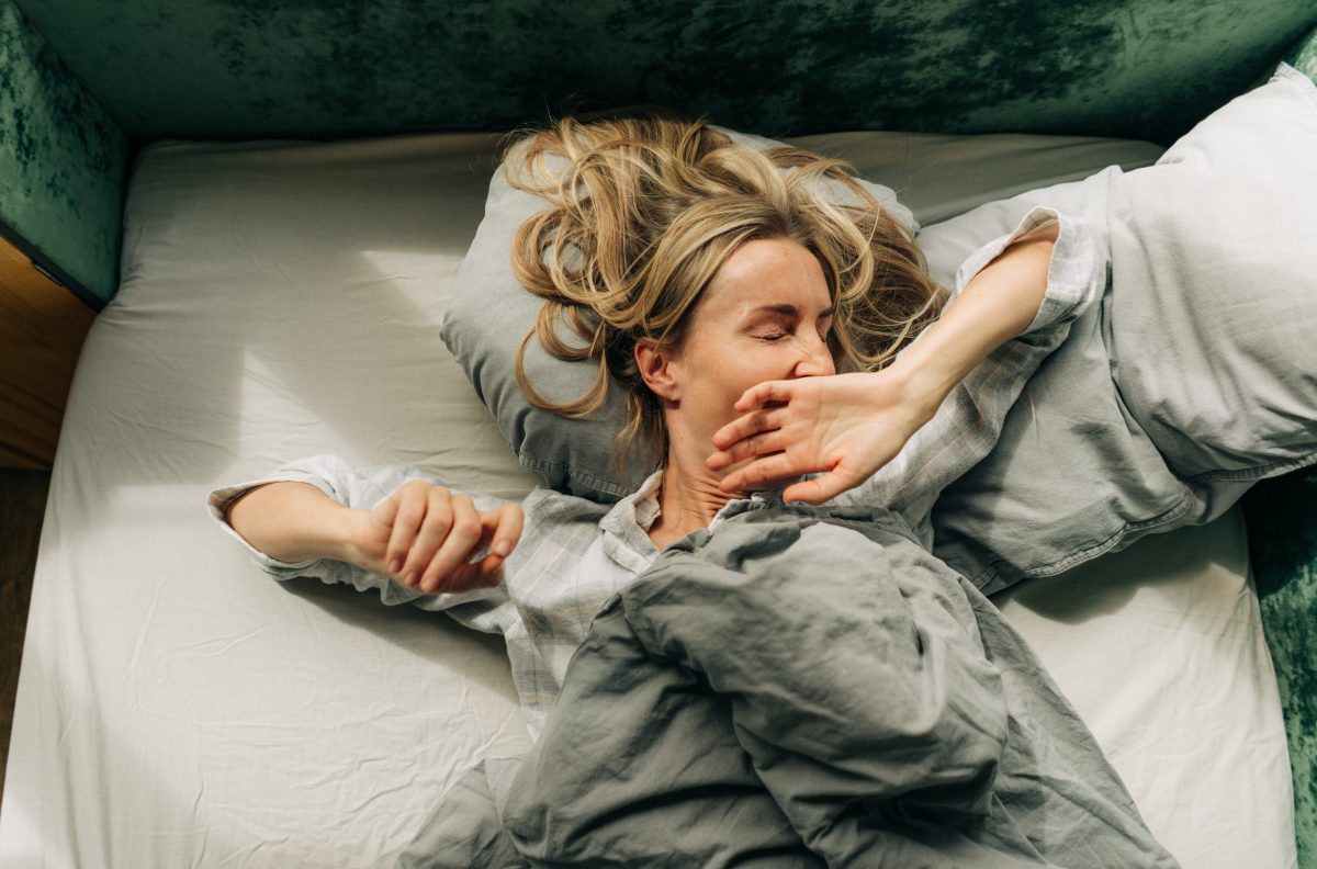 A woman after waking up stretches and yawns lying in bed in the morning.