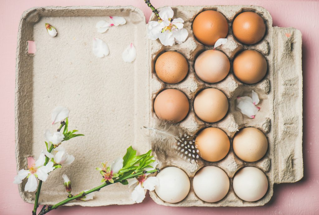 En kartong med ägg, fjädrar om äppelblommor på en rosa bordsskiva. 