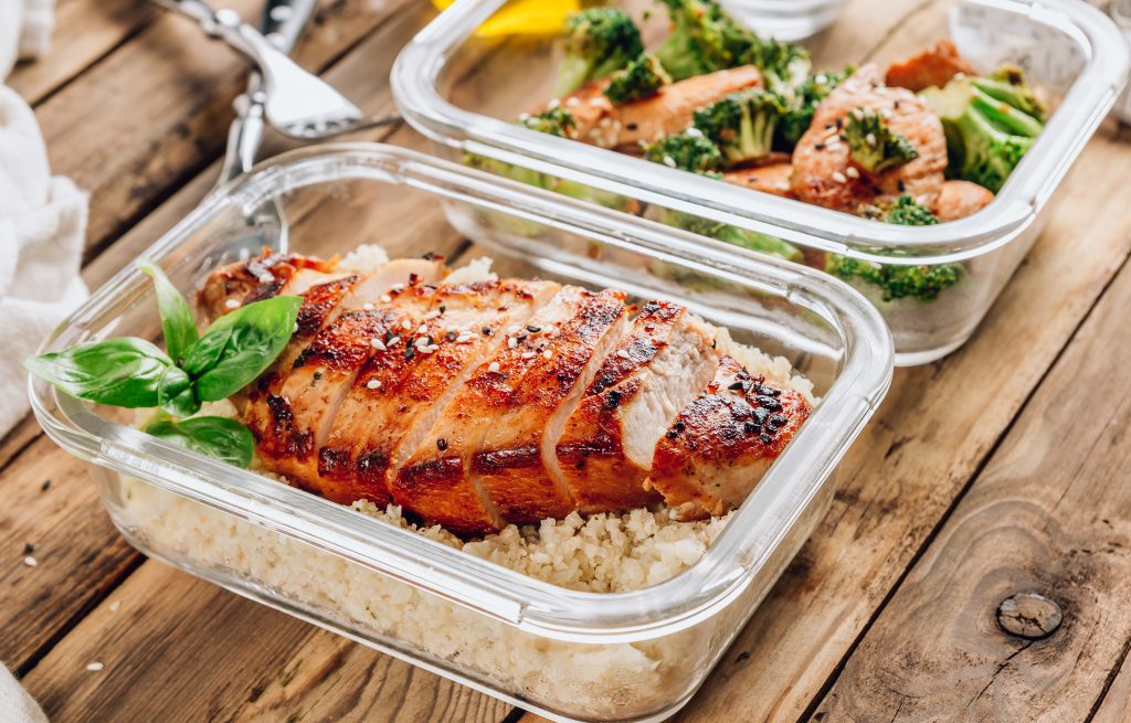 Keto lunchboxes - grilled chicken with cauliflower rice and chicken and broccoli in soy sauce with sesame seeds on a rustic wooden table. Top view