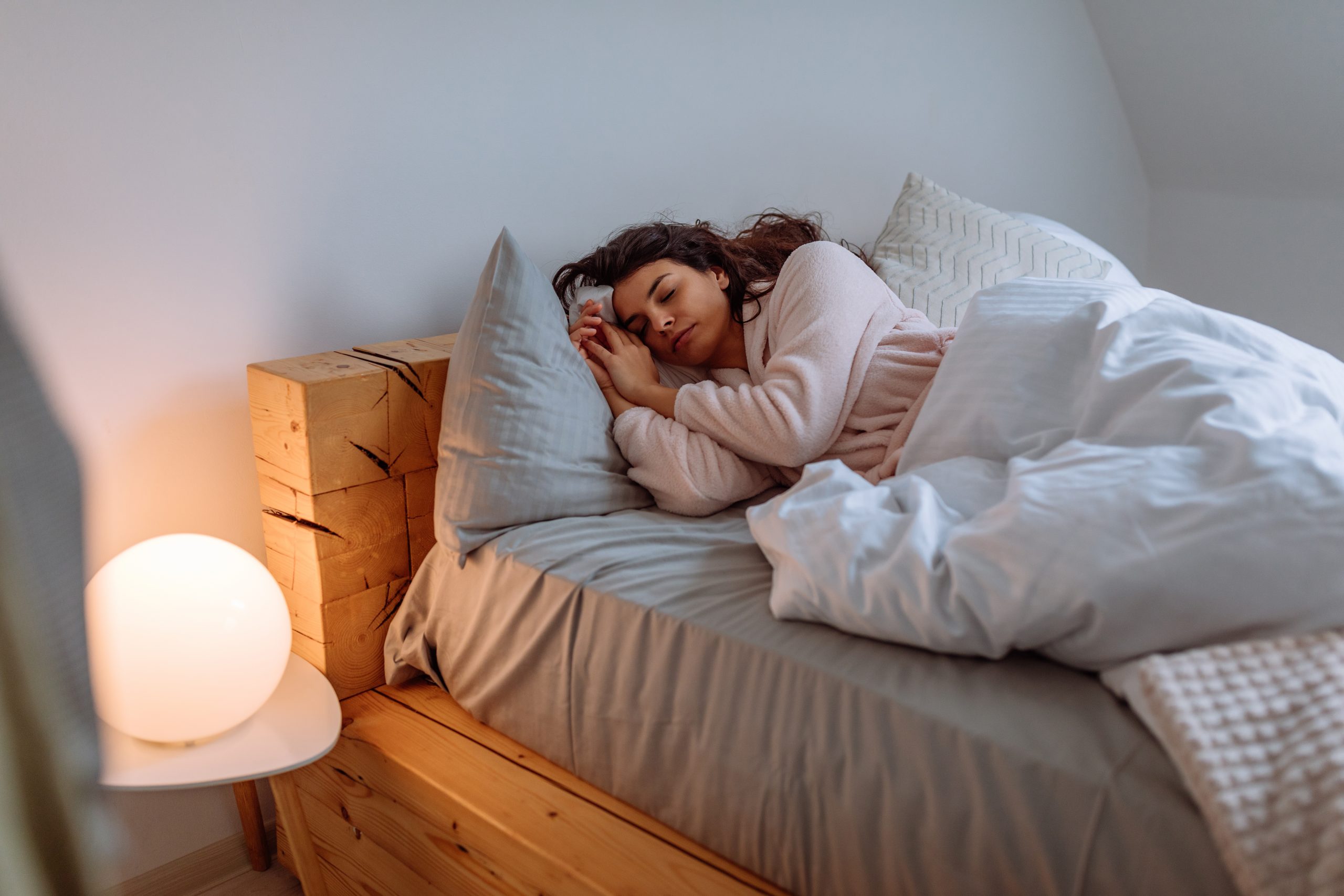 En ung kvinna sover i en säng med vita lakan.