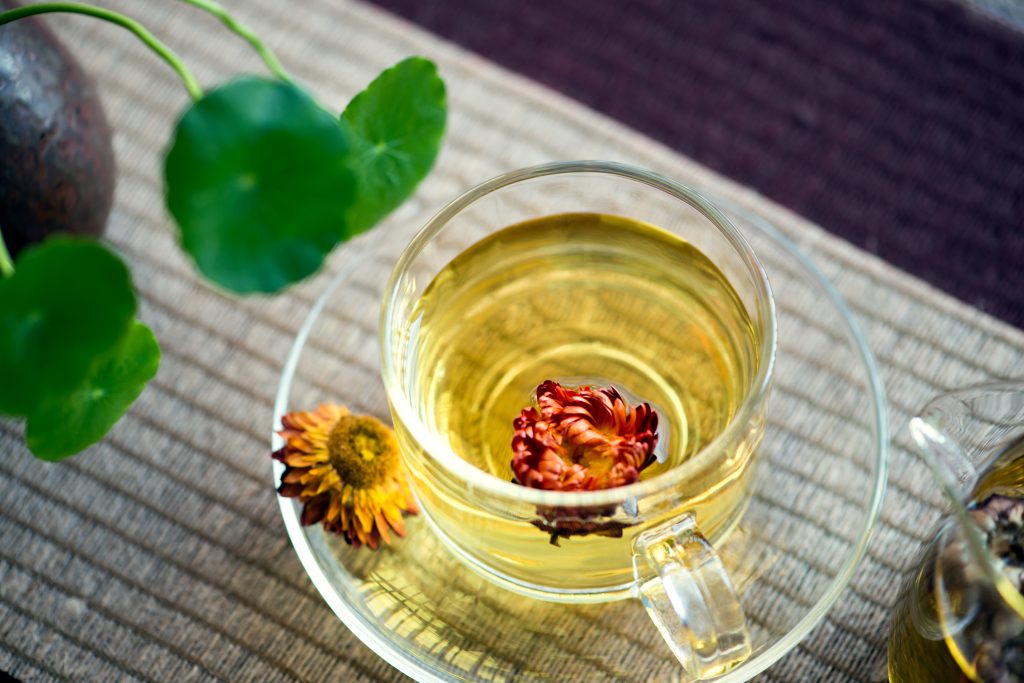 Tekopp i glas fyllt med blommor och örtte. 