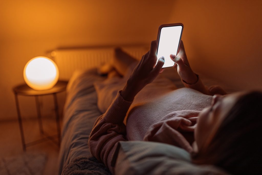 Young woman laying in bed and using her mobile phone before sleeping