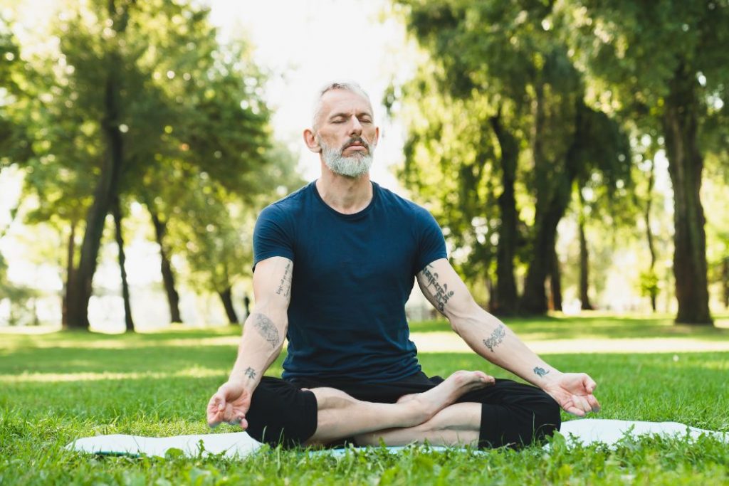 Man i 45-årsåldern mediterar på en gräsmatta. 
