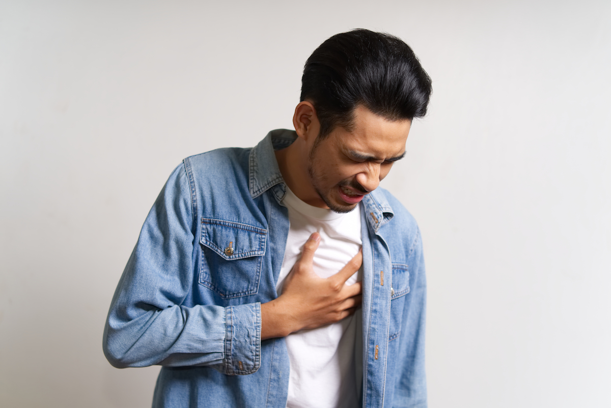 Foto på en man som håller handen över bröstet och ser ut att ha ont som om han får en hjärtinfarkt.