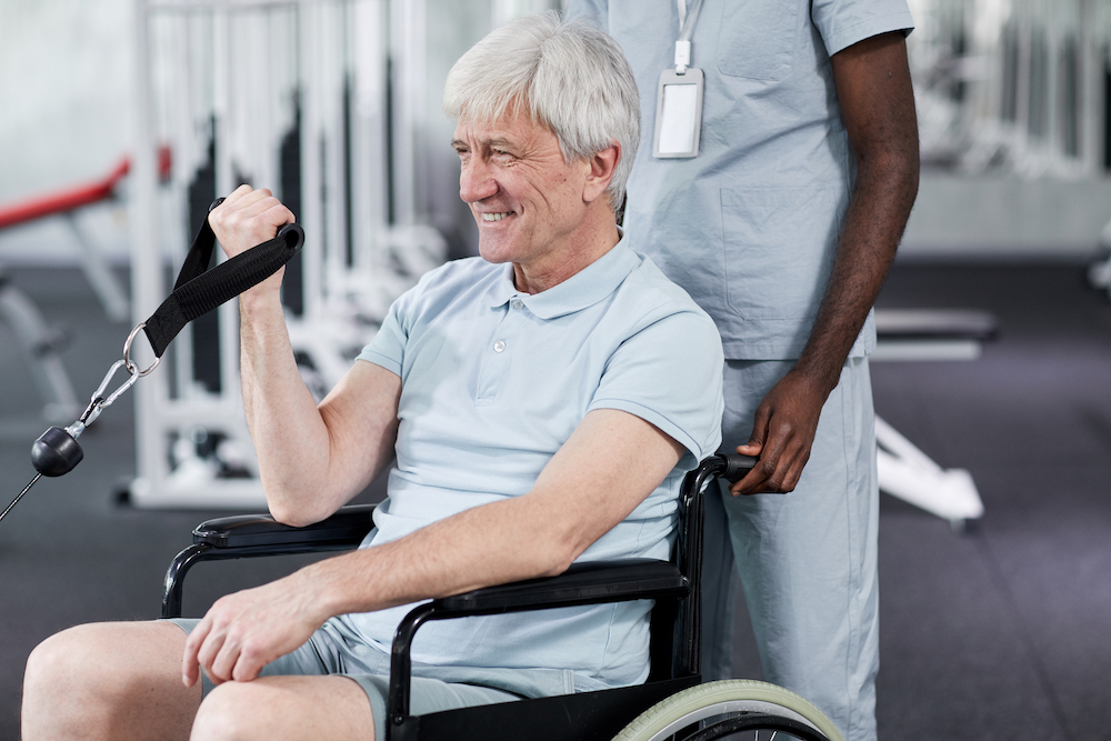 En man som sitter i en rullstol och kör en styrkeövning genom att hålla ett band.