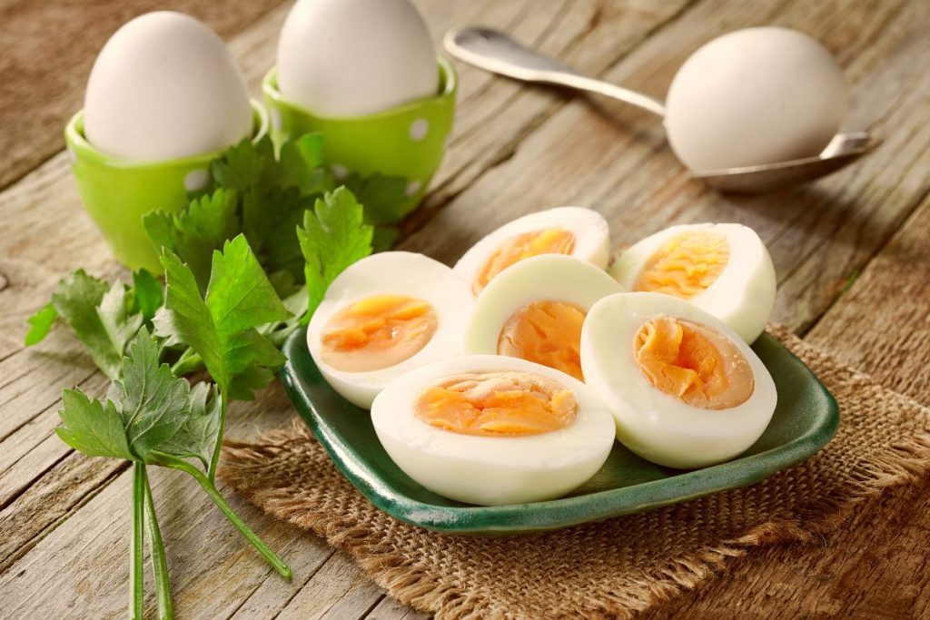 Ägghalvor liggandes på ett grönt fat, i bakgrunden finns två ägg i äggkoppar, ett ägg på en sked och bredvid ligger en kvist persilja.