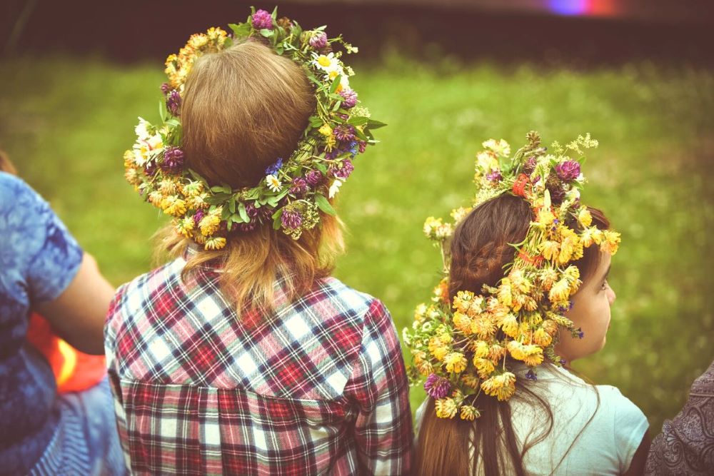 Två flickor sitter med ryggen mot kameran, iklädda blomsterkransar