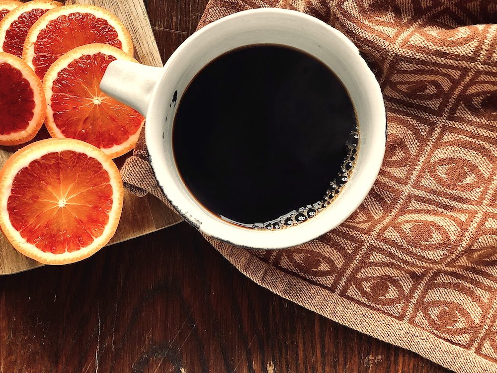 En kopp kaffe, en brun kökshandduk och några apelsinskivor på en skärbräda.