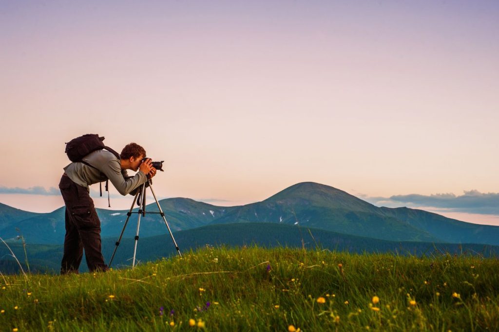Man som står på ett berg och fotograferar med sin kamera ståendes på ett stativ.