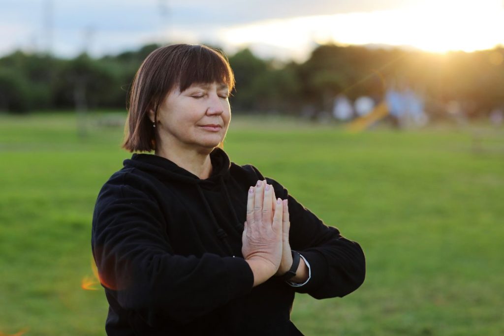Kvinna med kort brunt hår utövar meditation på en gräsmatt