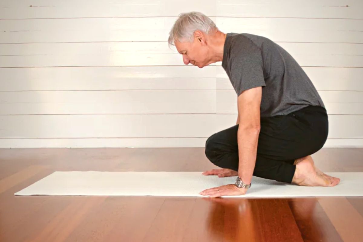 Äldre man i grå t-shirt och svarta byxor utövar yoga på en matta