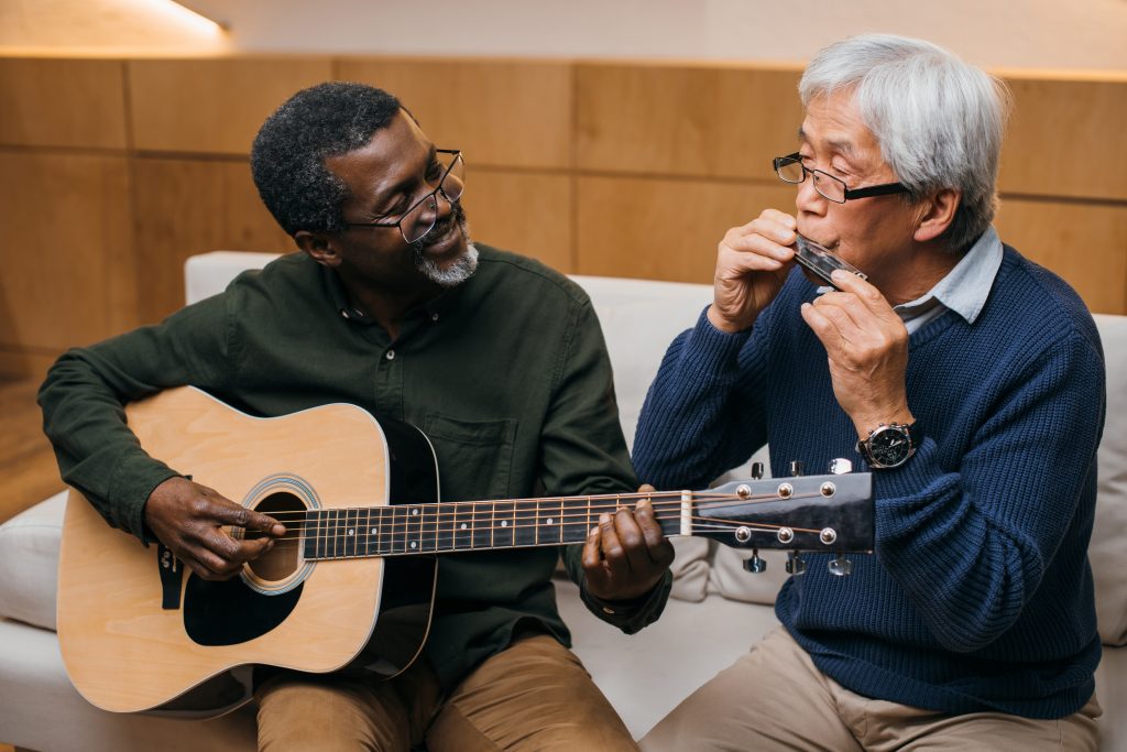 En svart man och en asiatisk man i 60-årsåldern spelar gitarr och munspel. 