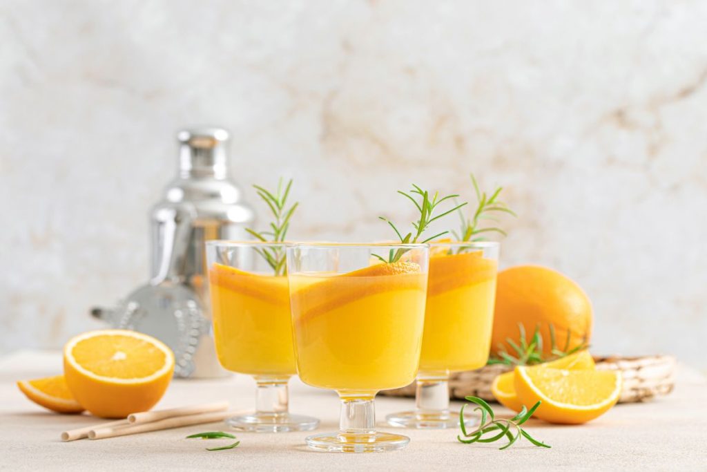 Glas på fot med apelsindrink, dekorerade med apelsinskivor och rosmarin