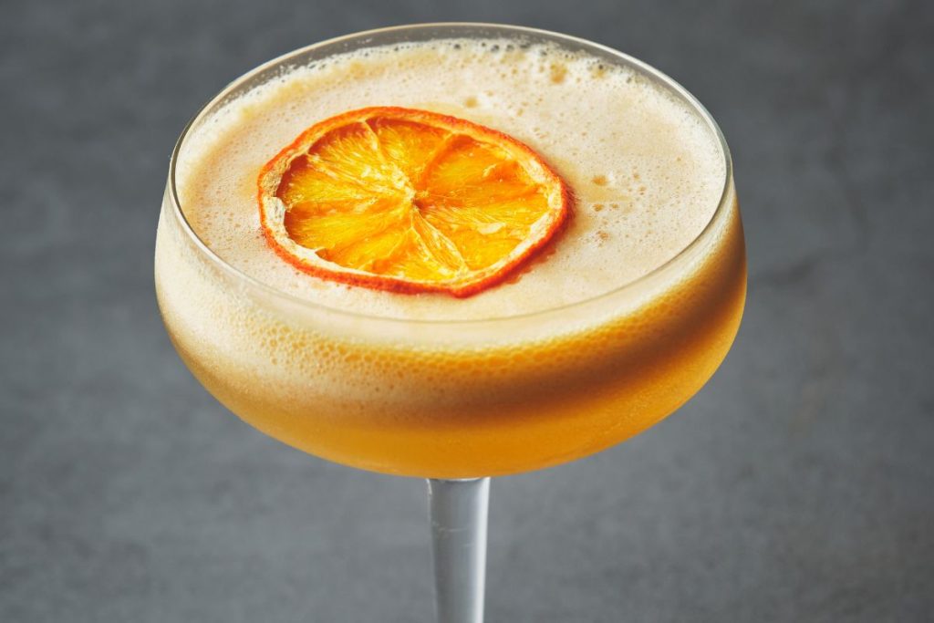 Cocktailglas med orange drink med skum och torkad apelsinskiva
