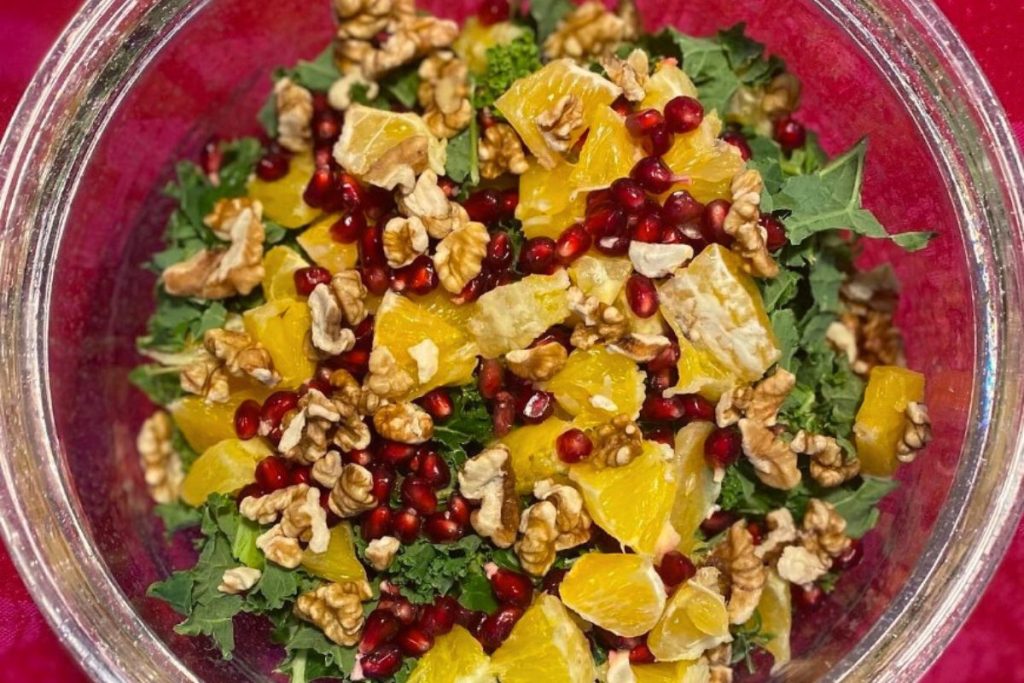 Grönkålssallad med apelsin, granatäplle och valnötter i en glasskål.