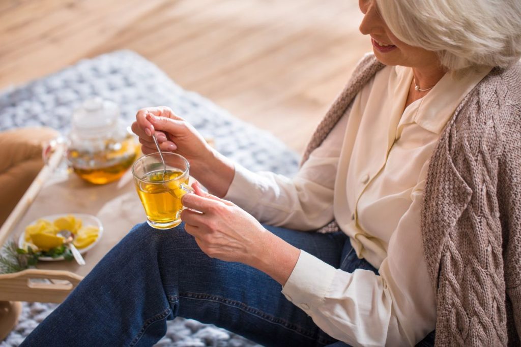 Vacker kvinna ca 50 år i blus och kofta dricker en kopp te på en matta
