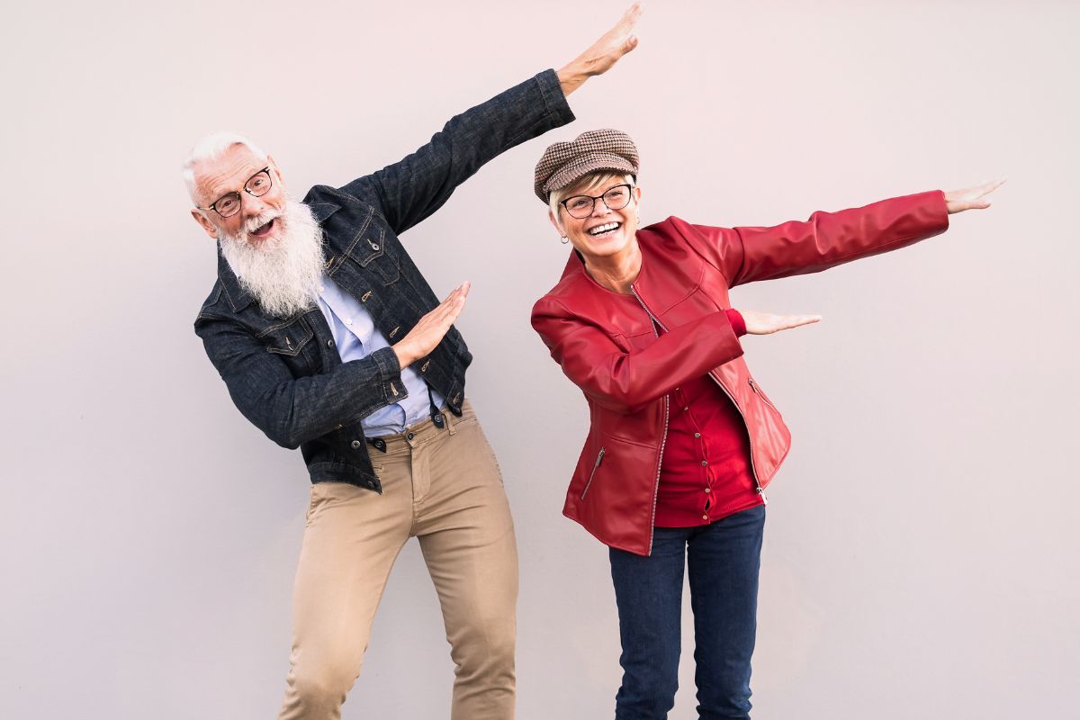 Stilig man och kvinna ca 65 år som dansar och spexar framför en vit vägg