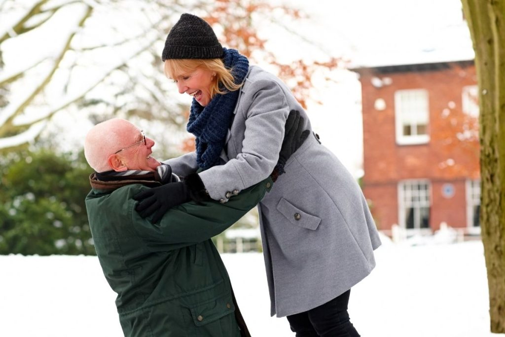 Man och kvinna, ca 65 år, busar i snön, mannen lyfter kvinnan i luften