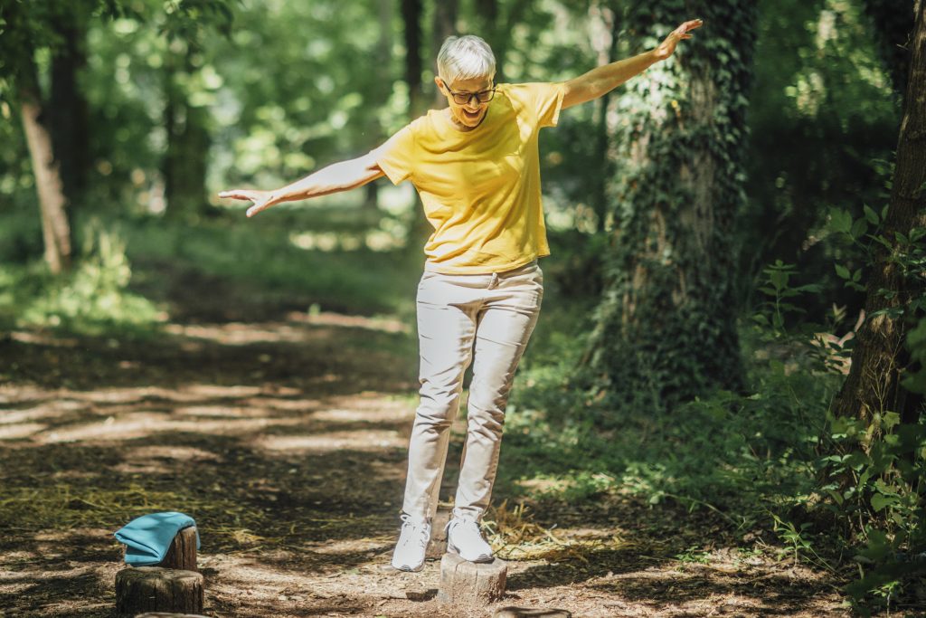 kvinna i gul tröja balanserar på en stock i skogen
