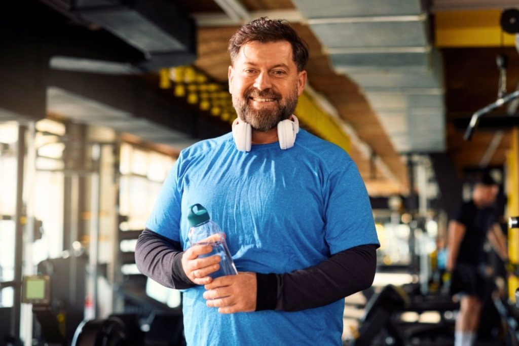 Man i blå t-shirt ler mot kameran på ett gym