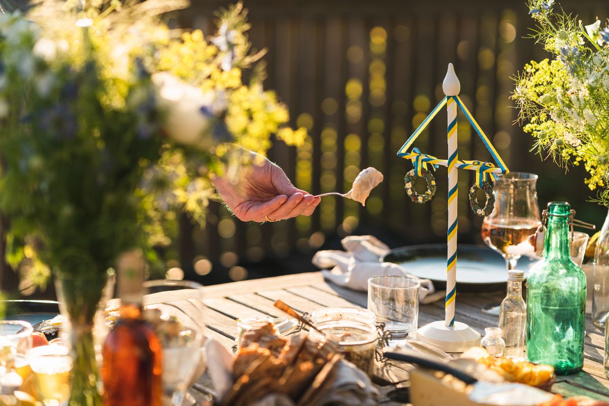 Närbild på en hand som tar en bit sill med en gaffel vid en midsommarbuffé.