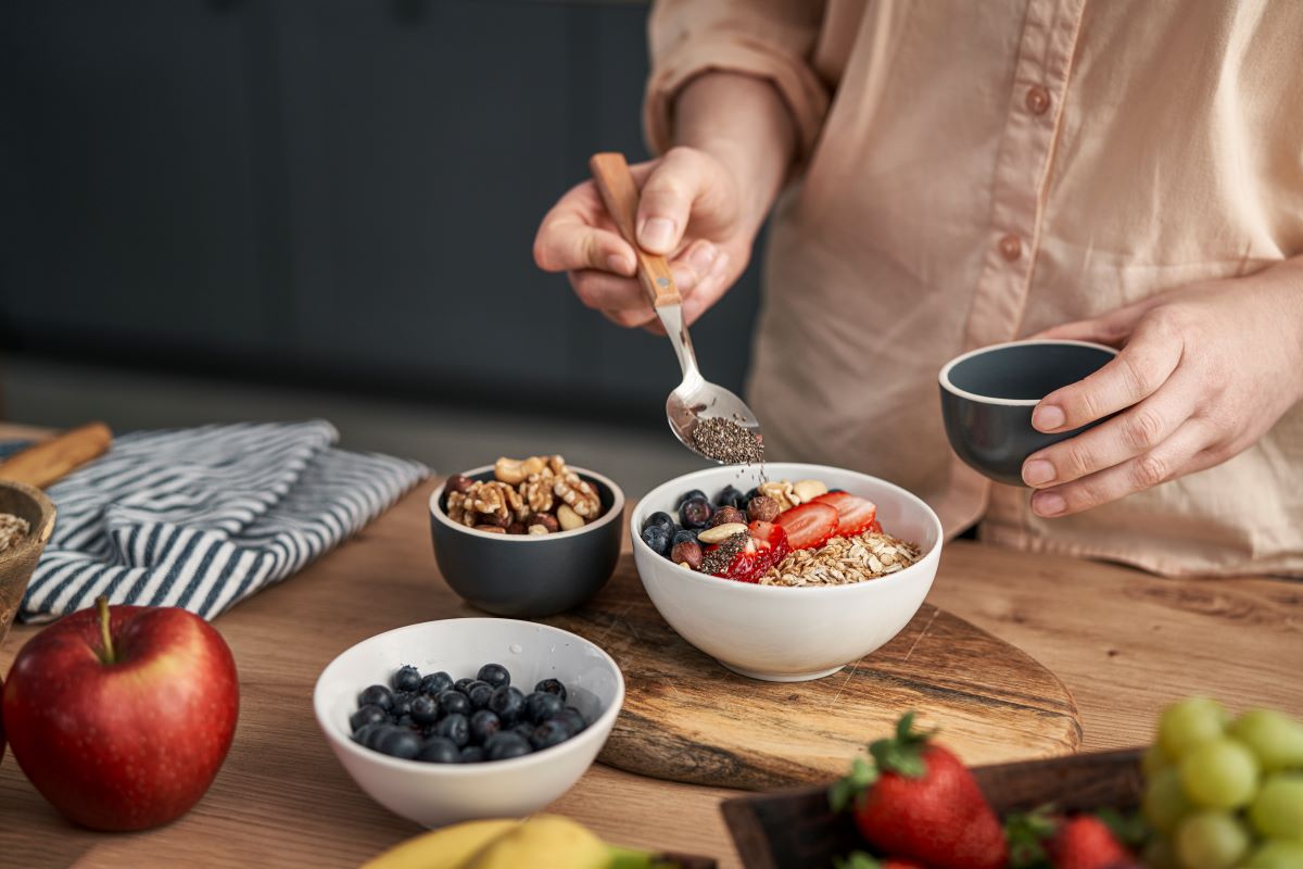 Kvinna toppar sin yoghurt med nötter och frukt vid en köksbänk