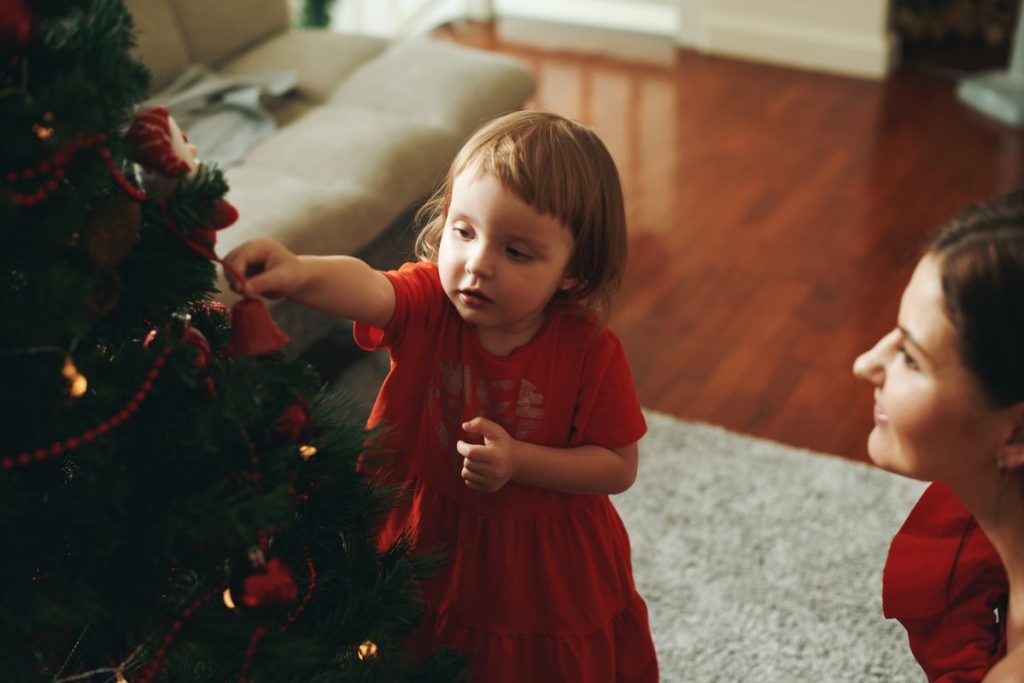 Liten flicka, ca 2 år, i röd klänning pyntar granen med sin mamma. 