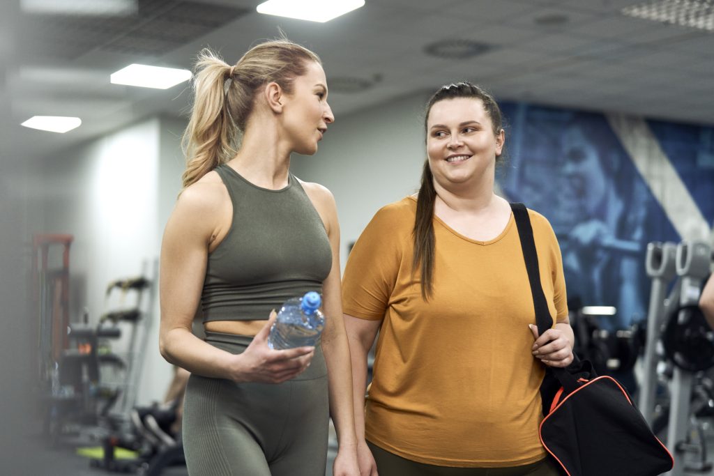 Två tjejkompisar, ca 30 år, pratar och ler medan de går ut från gymmet efter ett träningspass.