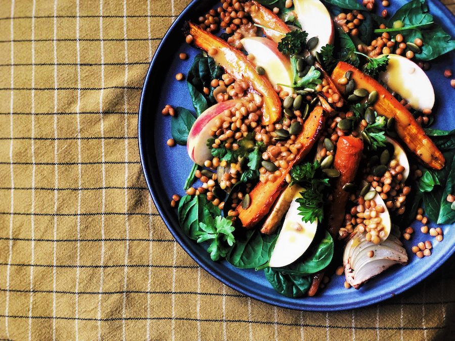 En grå tallrik med linssallad innehållandes morot, gröna linser, äpple, palsternacka och persilja.
