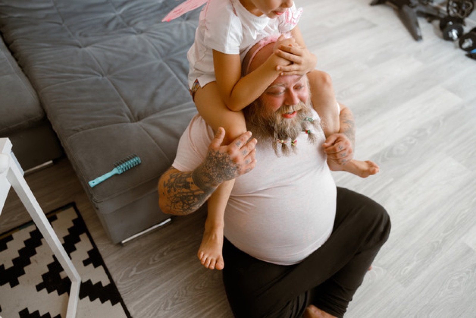 En man med skägg sitter på golvet med sin dotter på skuldrorna
