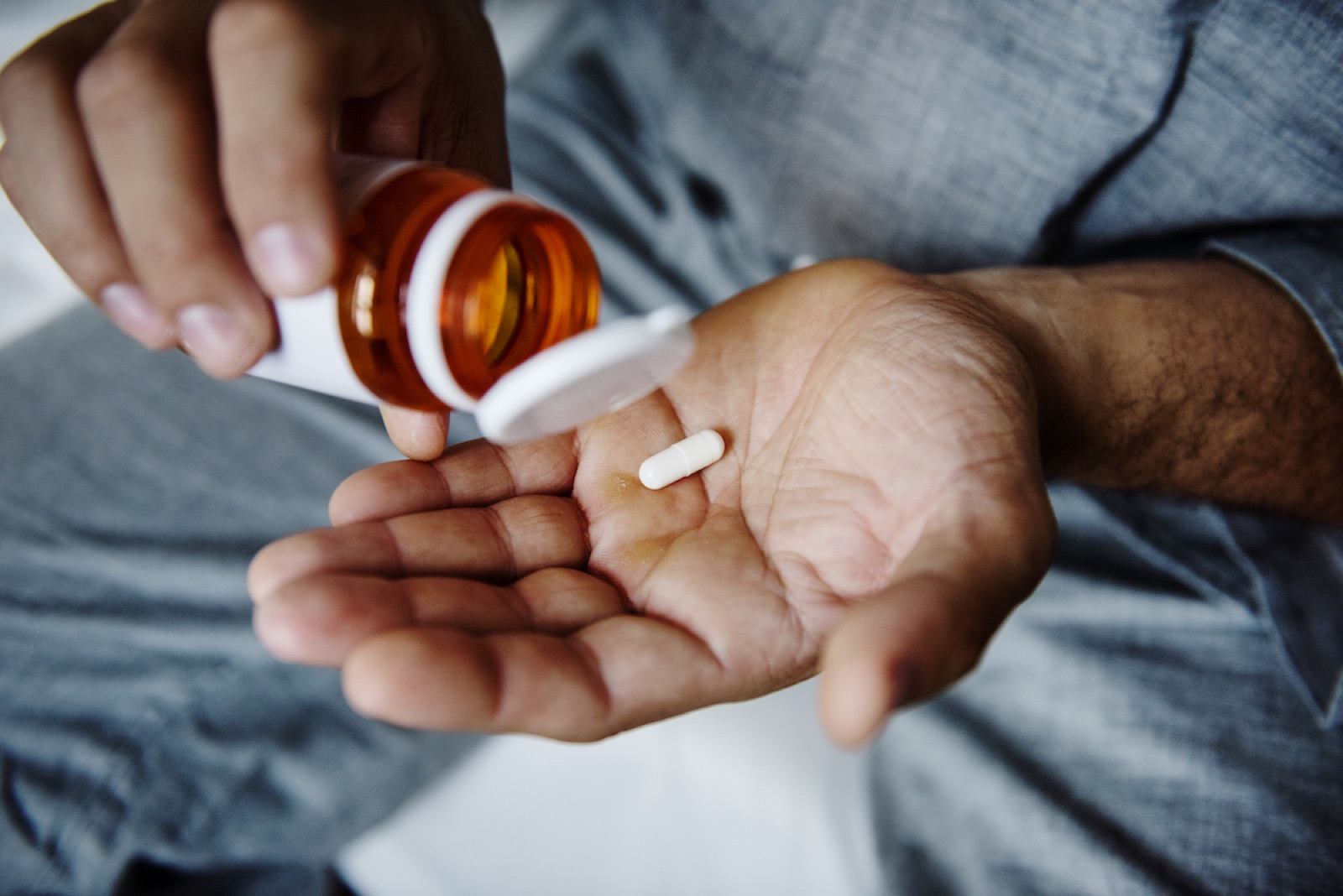 En person häller ut en tablett ur en medicinburk i handen
